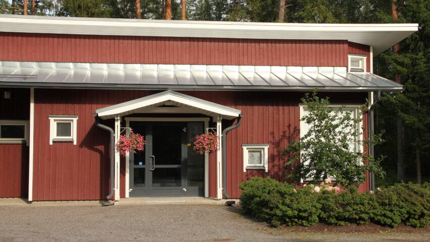 Punainen uudehko lautaseinäinen rakennus, jossa pieni katos ulko-oven edessä.