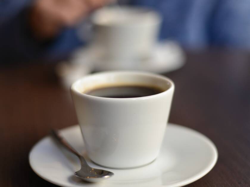 Pöydällä kaksi kahvikuppia. Vastapäätä istuu henkilö, jonka kädet näkyvät epäselvästi.