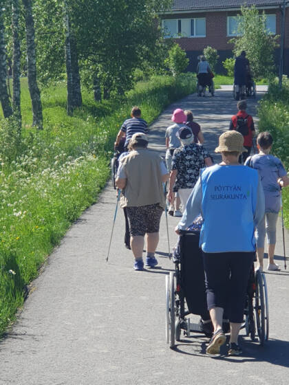 Iäkkäät ihmiset kulkevat kävelykatua pitkin selät kuvaajaa päin.