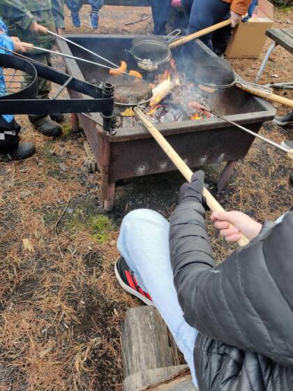 Nuotiolla paistetaan makkaraa, makkaratikkujen kanssa.