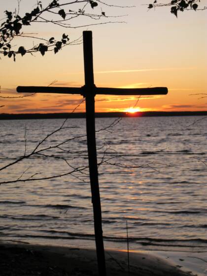 Puinen risti rannalla, jossa aurinko laskee.