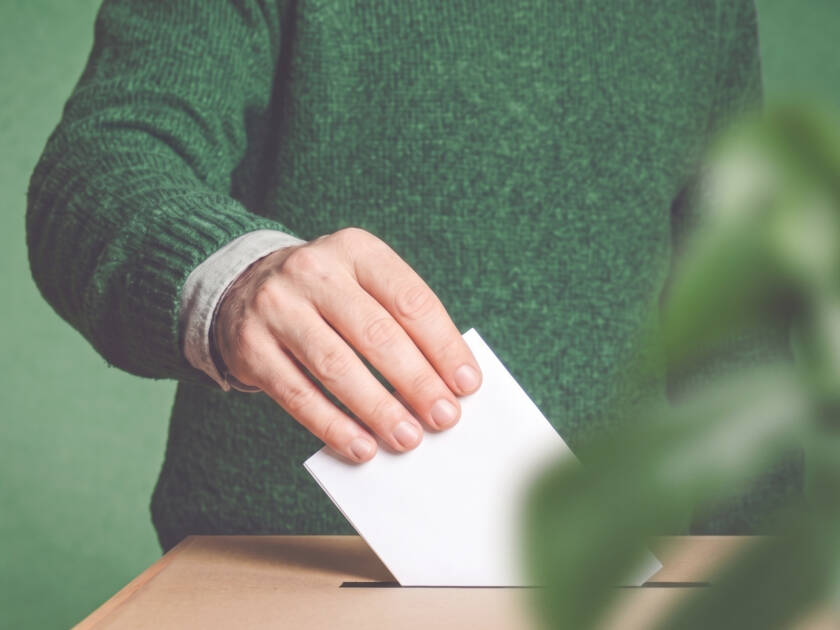 Miehen käsi laittaa äänestyslipuketta vaaliuurnaan.