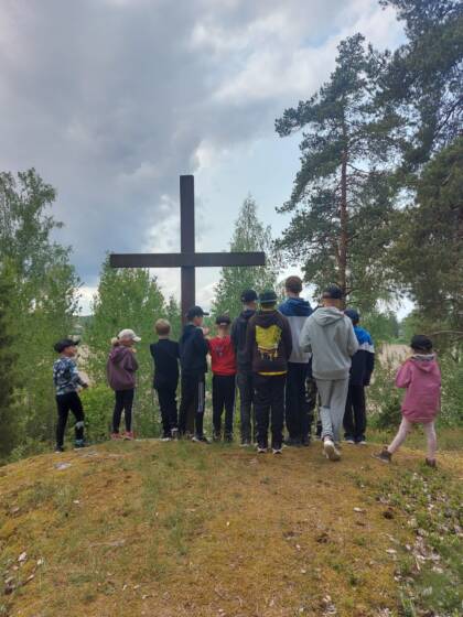 Nuoria ja lapsia seisomassa ison ristin vieressä luonnossa (Kappelniityn risti)