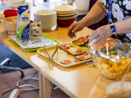 Kädet laittavat tarjoilupöydälle voileipiä, maitoa, astioita ja sipsejä.