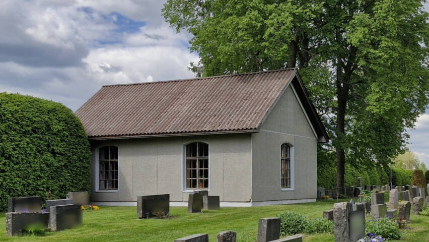 Pieni betonirapattu rakennus pikkuruutuikkunoin, vierellä iso lehtipuu.