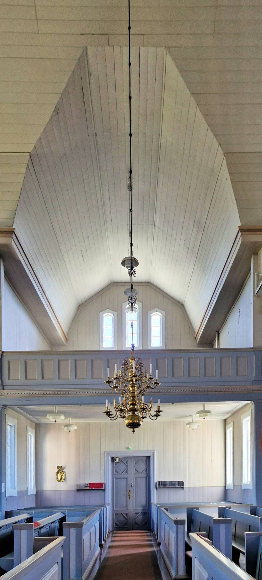 Näkymä kirkon sivuovelle, penkkirivistöineen ja parvella korkea katto.