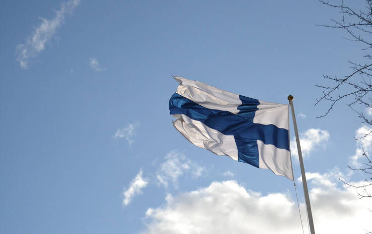 Suomen lippu liehuu sinitaivasta vasten.