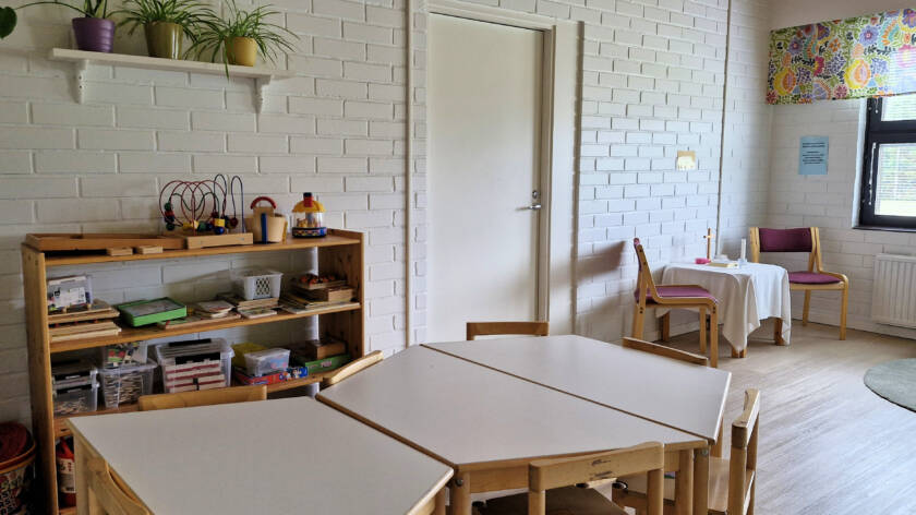 Matalat lasten pöydät ja tuolit sekä alttaripöytä, jossa kynttilä ja risti.