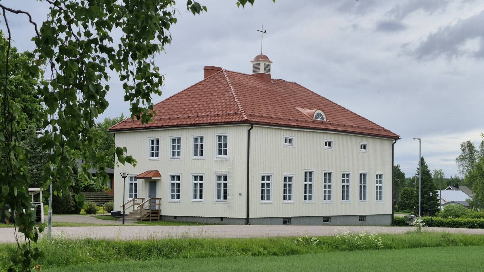 Kaksikerroksinen puutalo useine ikkunoineen, päädyssä portaat ja ovi.