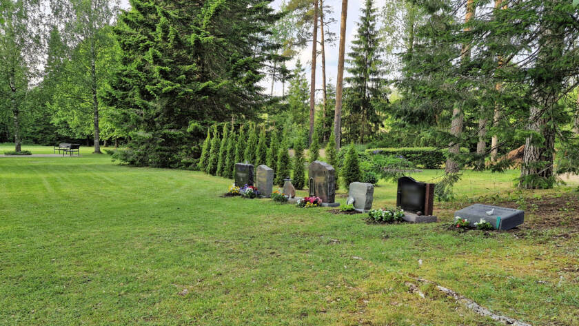 Hautausmaalla nurmikon reunassa muistokiviä sekä havupuita.