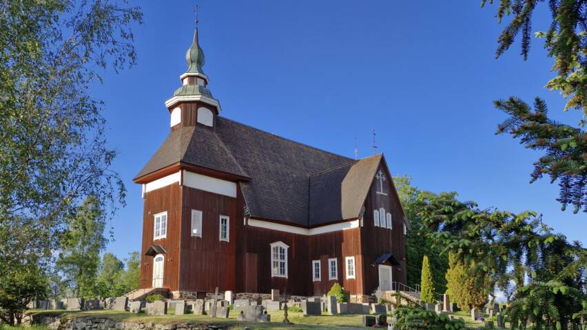 Puinen ristikirkko mäen päällä hautausmaan ympäröimä.
