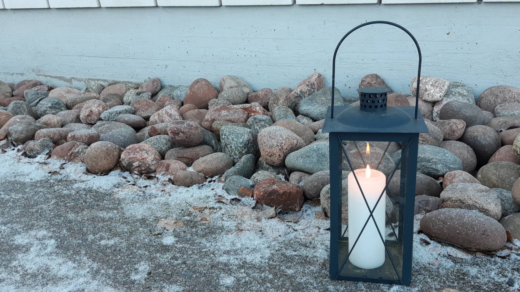 Kynttilä palaa valkoisessa lyhdyssä ulkona.