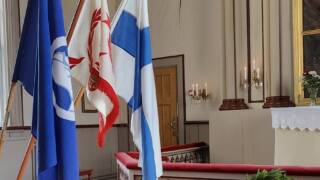 Kirkon alttarikaiteen vieressä Suomen lippu ja veteraanijärjestöjen liput.